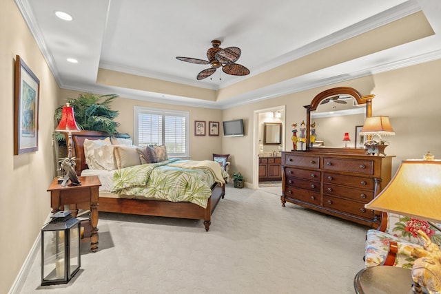 bedroom featuring connected bathroom, a tray ceiling, ornamental molding, ceiling fan, and light carpet