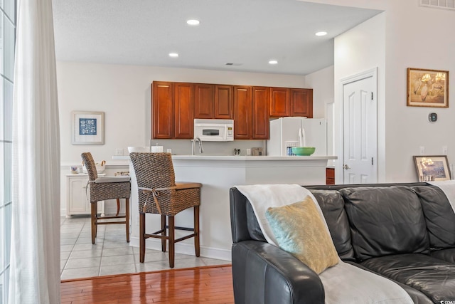 kitchen with a breakfast bar, sink, white appliances, and light hardwood / wood-style flooring