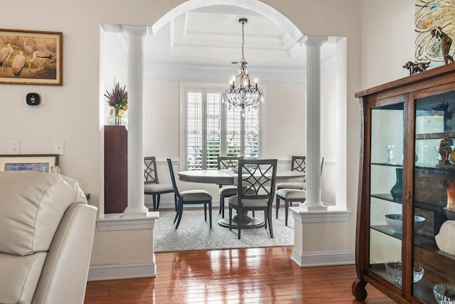 dining area featuring hardwood / wood-style flooring, ornamental molding, an inviting chandelier, and ornate columns