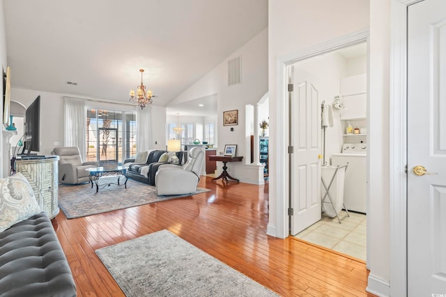 living room with washer / clothes dryer, high vaulted ceiling, an inviting chandelier, and light hardwood / wood-style floors