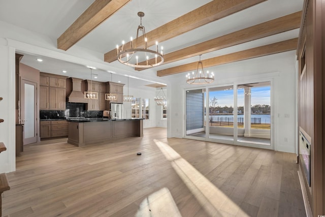 kitchen with light wood finished floors, custom exhaust hood, dark countertops, open floor plan, and a chandelier