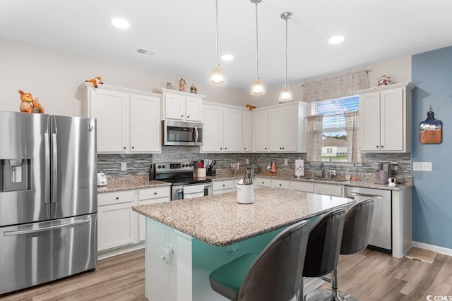 kitchen featuring stainless steel appliances, a kitchen island, white cabinets, and decorative light fixtures