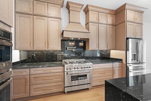 kitchen featuring light hardwood / wood-style flooring, appliances with stainless steel finishes, dark stone countertops, tasteful backsplash, and custom range hood