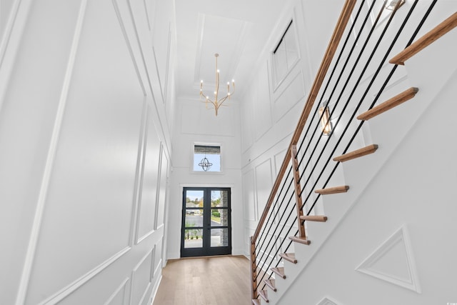 foyer featuring french doors, a towering ceiling, a chandelier, and light wood-type flooring