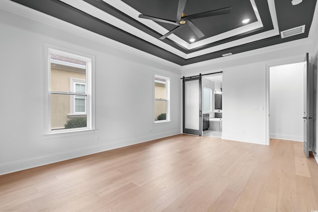 spare room featuring a tray ceiling, light hardwood / wood-style flooring, a barn door, and plenty of natural light