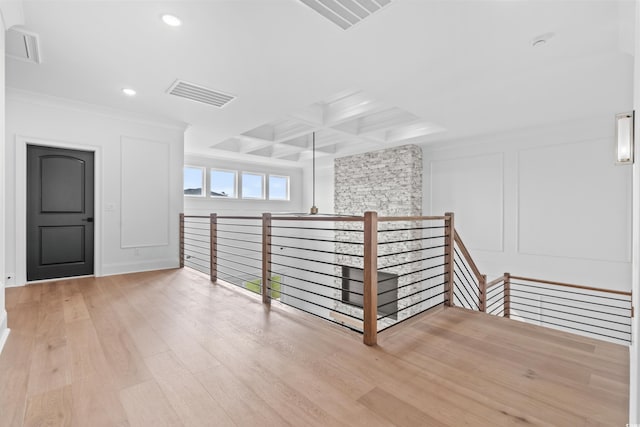 interior space with beam ceiling, ornamental molding, coffered ceiling, and light hardwood / wood-style floors