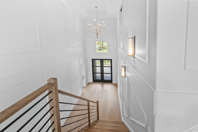 entrance foyer with crown molding, a towering ceiling, light hardwood / wood-style floors, french doors, and a chandelier