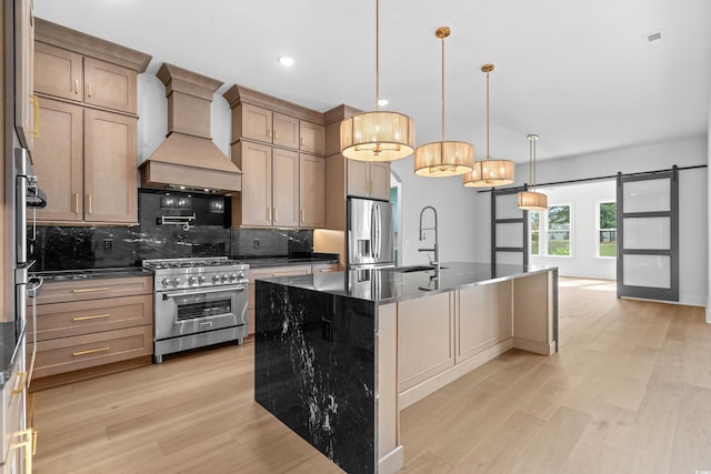 kitchen with premium range hood, an island with sink, hanging light fixtures, stainless steel appliances, and a barn door