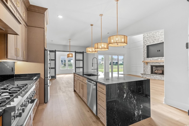 kitchen with sink, appliances with stainless steel finishes, dark stone countertops, a barn door, and a large island with sink