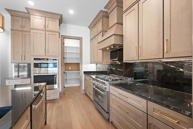 kitchen with stainless steel appliances, custom range hood, light hardwood / wood-style flooring, and dark stone counters