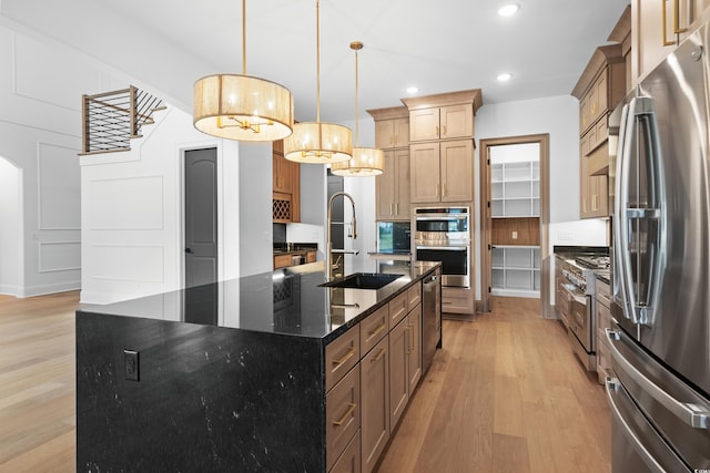 kitchen with sink, a kitchen island with sink, dark stone countertops, stainless steel appliances, and decorative light fixtures