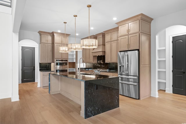 kitchen with an island with sink, appliances with stainless steel finishes, sink, and decorative light fixtures