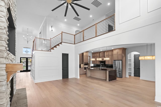 kitchen with pendant lighting, stainless steel fridge, a kitchen island with sink, ceiling fan with notable chandelier, and light wood-type flooring