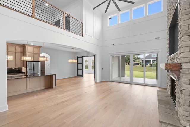 unfurnished living room featuring a stone fireplace, sink, a chandelier, light hardwood / wood-style flooring, and a towering ceiling