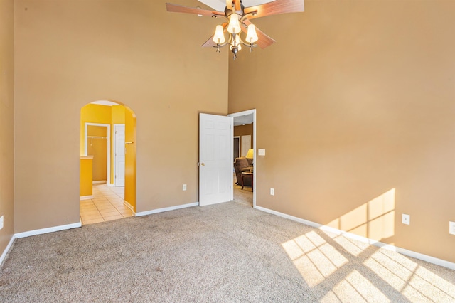 unfurnished bedroom with ceiling fan, light colored carpet, connected bathroom, and a towering ceiling