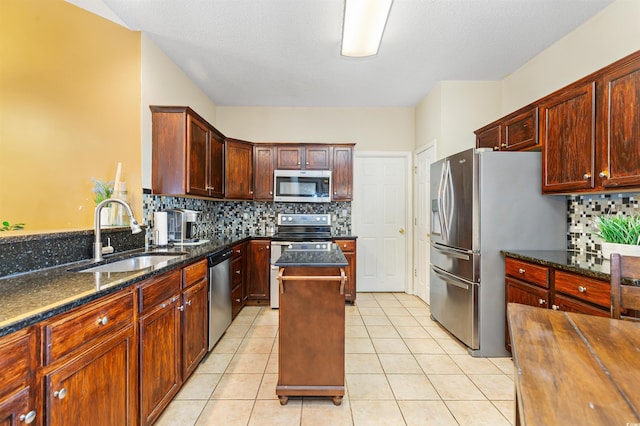 kitchen featuring sink, a center island, dark stone countertops, light tile patterned floors, and appliances with stainless steel finishes