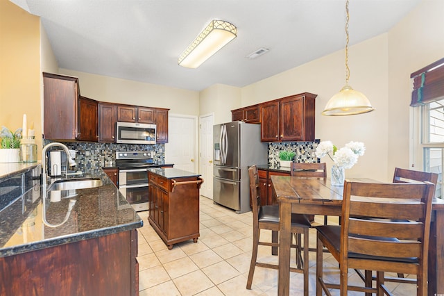 kitchen featuring light tile patterned flooring, sink, dark stone counters, a kitchen island, and stainless steel appliances