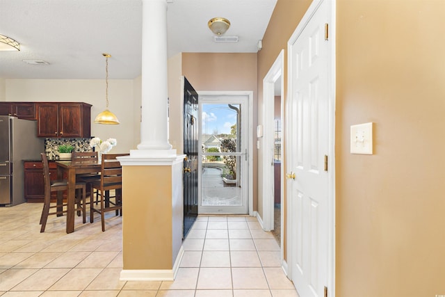 interior space featuring pendant lighting, stainless steel refrigerator, backsplash, decorative columns, and light tile patterned flooring