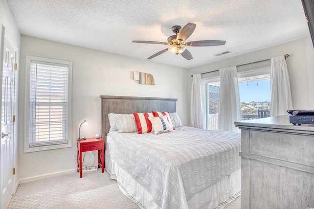 carpeted bedroom with a textured ceiling, baseboards, visible vents, and ceiling fan