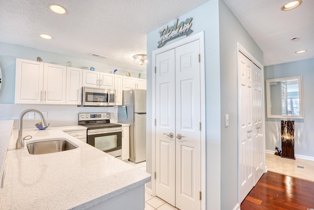 kitchen featuring light stone counters, appliances with stainless steel finishes, white cabinets, a textured ceiling, and a sink