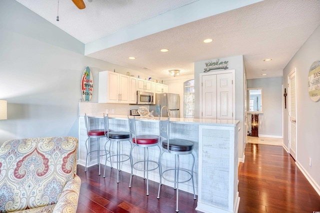 kitchen featuring light countertops, a kitchen breakfast bar, a peninsula, stainless steel appliances, and dark wood-style flooring