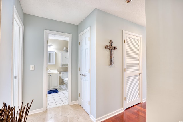 hall featuring light tile patterned floors, a textured ceiling, and baseboards