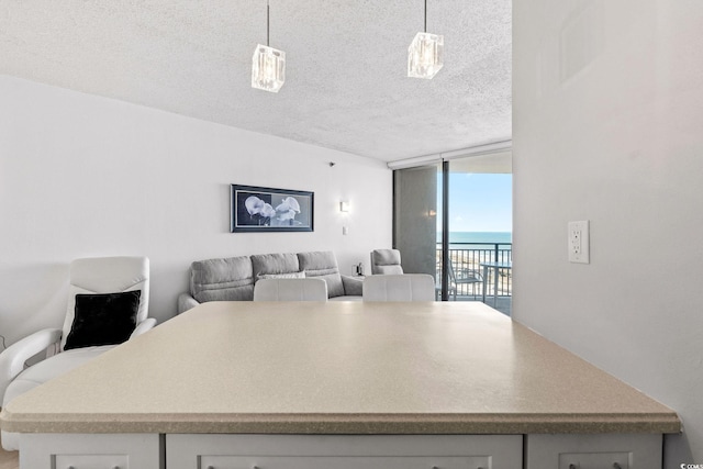 kitchen featuring hanging light fixtures, a water view, a textured ceiling, and expansive windows