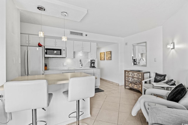 kitchen featuring light tile patterned flooring, a breakfast bar, tasteful backsplash, refrigerator, and pendant lighting