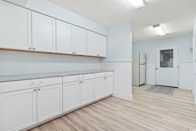 3545 Marion Ln, Murrells Inlet, SC 29576 - kitchen featuring freestanding refrigerator, a textured ceiling, light wood-style floors, white cabinetry, and baseboards