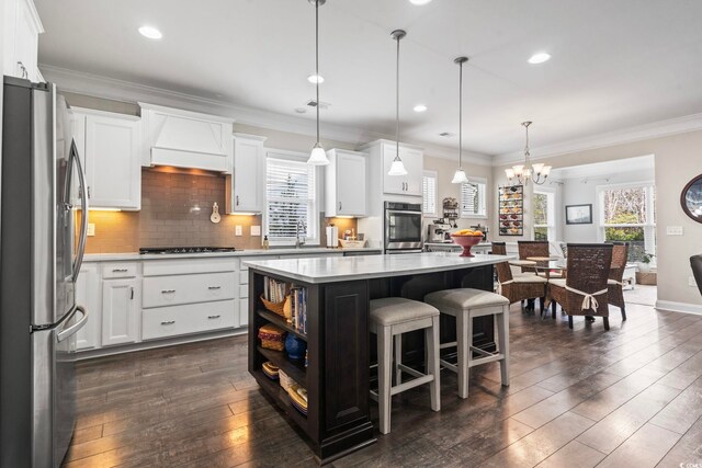 kitchen featuring stainless steel appliances, an island with sink, hanging light fixtures, and white cabinetry