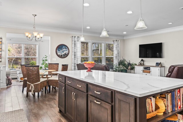 kitchen with dark wood-type flooring, dark brown cabinets, ornamental molding, pendant lighting, and light stone countertops