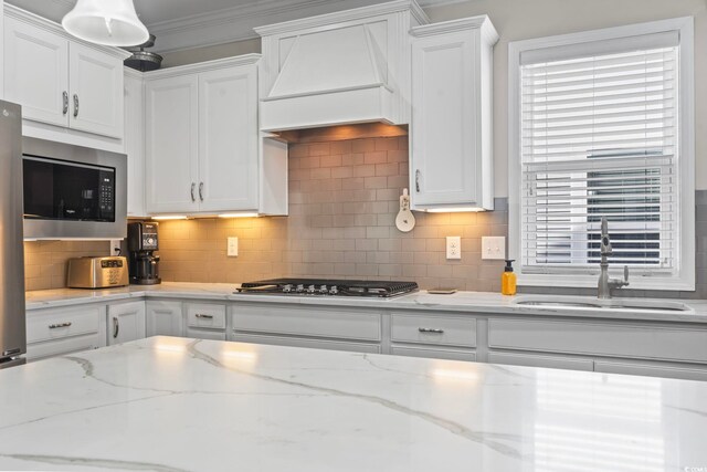 kitchen with premium range hood, stainless steel gas stovetop, black microwave, white cabinetry, and sink