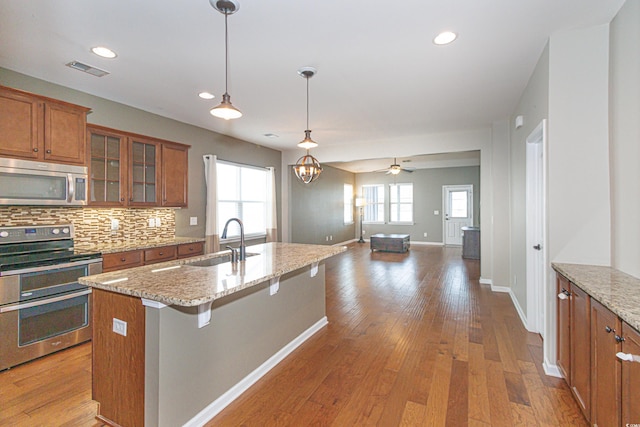 kitchen with appliances with stainless steel finishes, decorative light fixtures, sink, a kitchen breakfast bar, and light stone countertops