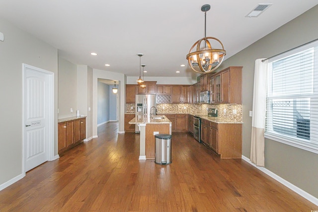 kitchen with sink, appliances with stainless steel finishes, a kitchen island with sink, a kitchen bar, and decorative light fixtures