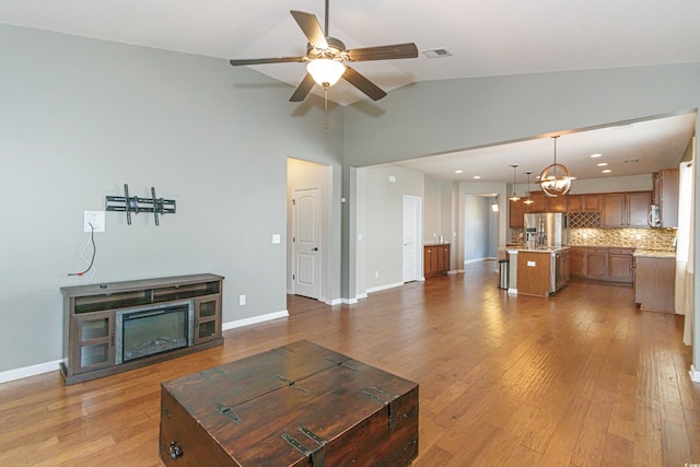 living room with lofted ceiling, ceiling fan with notable chandelier, and light wood-type flooring