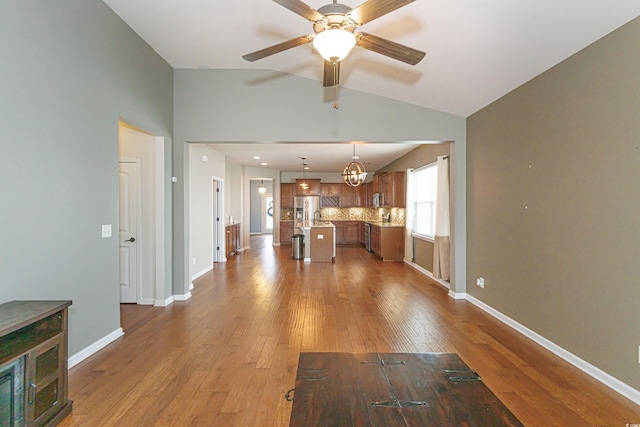 unfurnished living room featuring hardwood / wood-style flooring, ceiling fan with notable chandelier, and vaulted ceiling