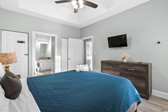 bedroom featuring ceiling fan, connected bathroom, a raised ceiling, and light wood-type flooring