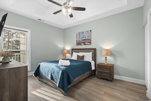 bedroom featuring light hardwood / wood-style floors, a raised ceiling, and ceiling fan