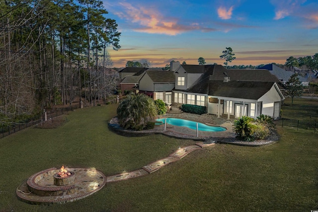 pool at dusk featuring a fire pit and a lawn