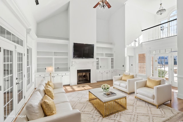 living room with french doors, light hardwood / wood-style flooring, built in features, ceiling fan, and a high ceiling