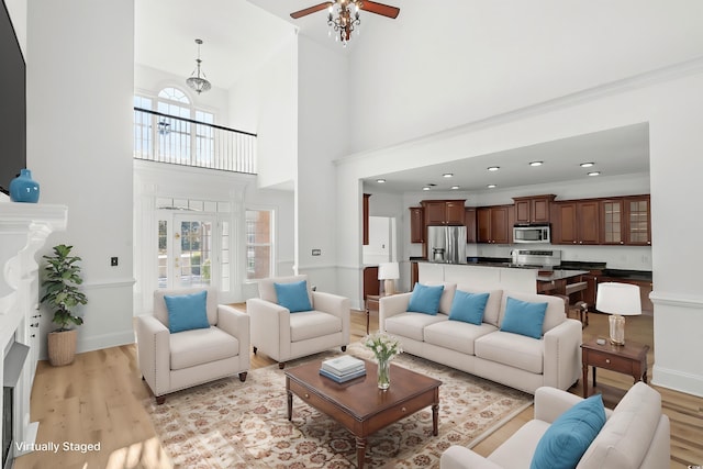 living room with a towering ceiling, light hardwood / wood-style flooring, ornamental molding, and ceiling fan