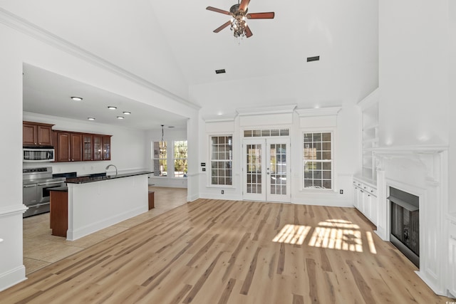 unfurnished living room featuring french doors, sink, crown molding, high vaulted ceiling, and light hardwood / wood-style floors