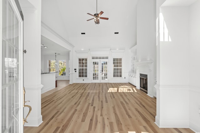 unfurnished living room featuring a high ceiling, ceiling fan, light hardwood / wood-style floors, and french doors