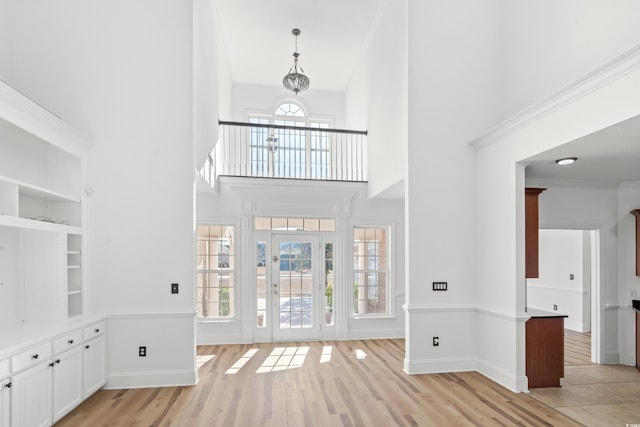 foyer entrance with a towering ceiling, light hardwood / wood-style flooring, ornamental molding, and a chandelier