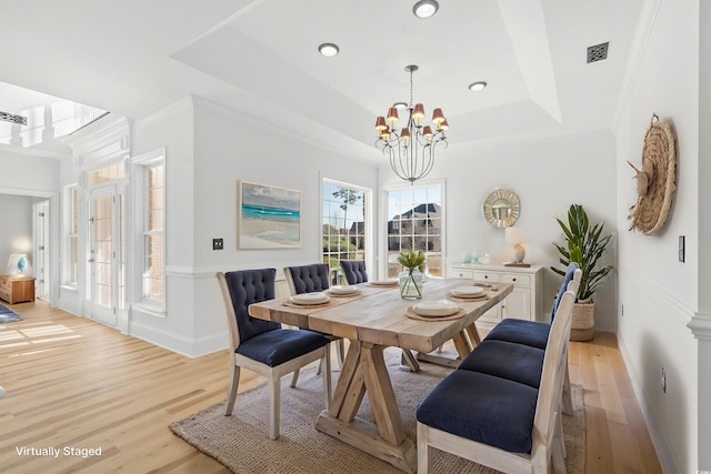 dining space featuring crown molding, a tray ceiling, a chandelier, and light hardwood / wood-style flooring