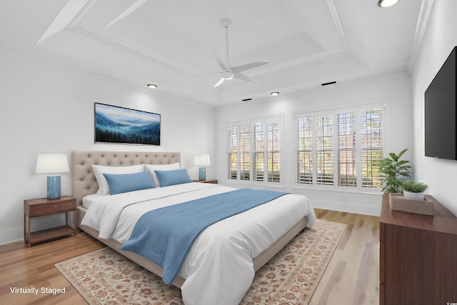 bedroom with ornamental molding, ceiling fan, light wood-type flooring, and a tray ceiling