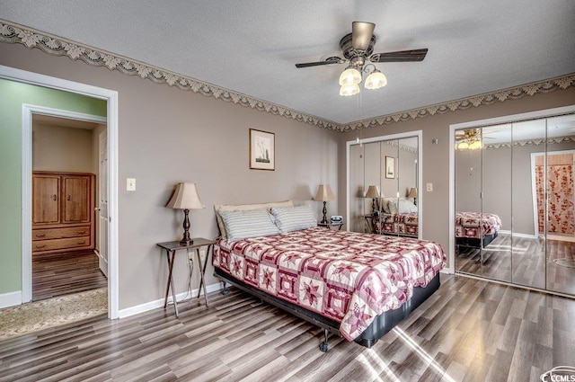 bedroom with ceiling fan, hardwood / wood-style floors, a textured ceiling, and two closets