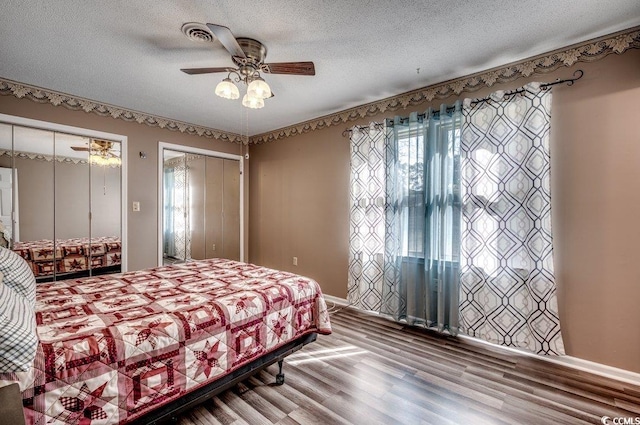 bedroom featuring hardwood / wood-style floors, ceiling fan, two closets, and a textured ceiling