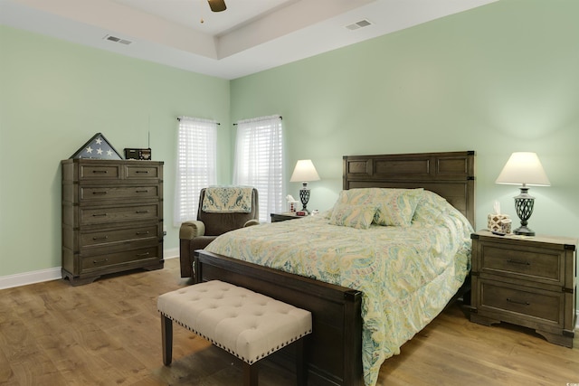 bedroom featuring ceiling fan, a tray ceiling, and light hardwood / wood-style flooring