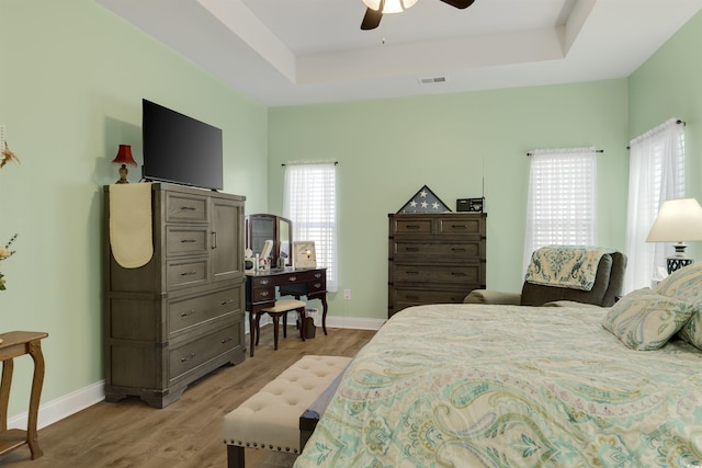 bedroom with ceiling fan, a tray ceiling, and light hardwood / wood-style floors